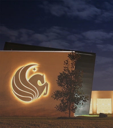 The UCF logo illuminated on a campus building at night